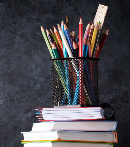 Colored pencils and a ruler in a container on top of stacked books