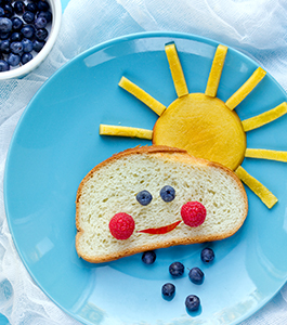 Fruit in the shape of a sun and bread in the shape of a cloud with a smiley face formed by fruit