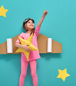 Girl dressed in an airplane and pilot costume holds up her fist as her other hand holds a star pillow